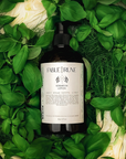 Bottle of Fable Truue lotion surrounded by green basil leaves and fennel bulbs