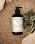 Bottle of Fable & Rune product on sand with a plant and shell