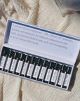 A set of travel size perfume rollers displayed in a box, with each roller labeled with different fragrance names like Bergamot & Black Pepper, Be Well, Herbarium, and others.
