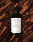 Bottle of Fable & Rune product surrounded by cinnamon sticks and star anise on a dark background