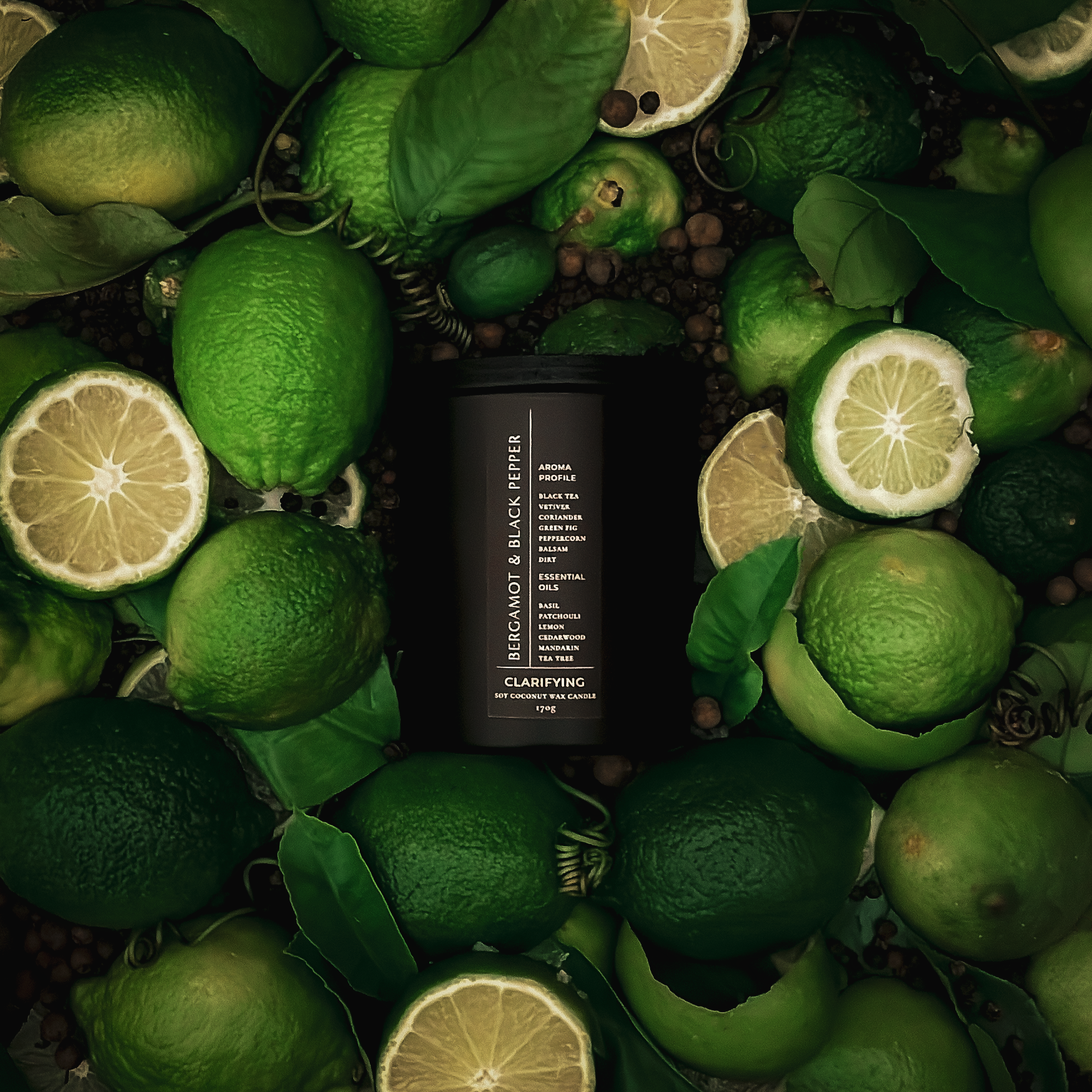 Black cylindrical candle surrounded by green bergamot citrus and leaves