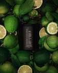 Black cylindrical candle surrounded by green bergamot citrus and leaves