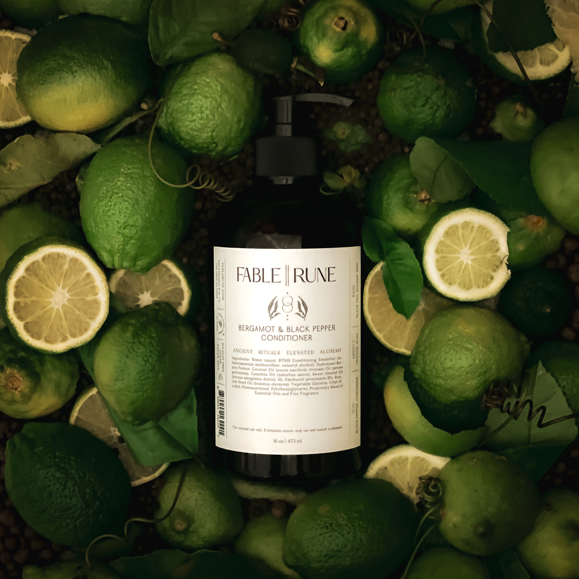 Bottle of Fable & Rune soap surrounded by bergamot citrus and leaves on a dark background