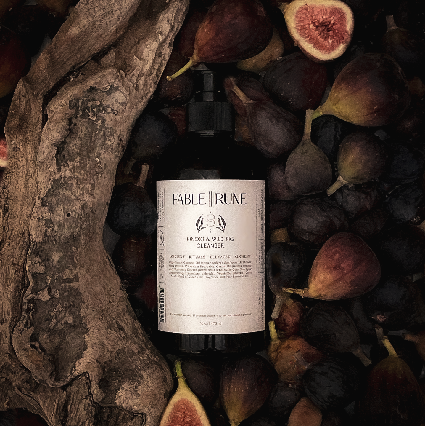 Bottle of body cleanser product surrounded by figs and natural wood elements