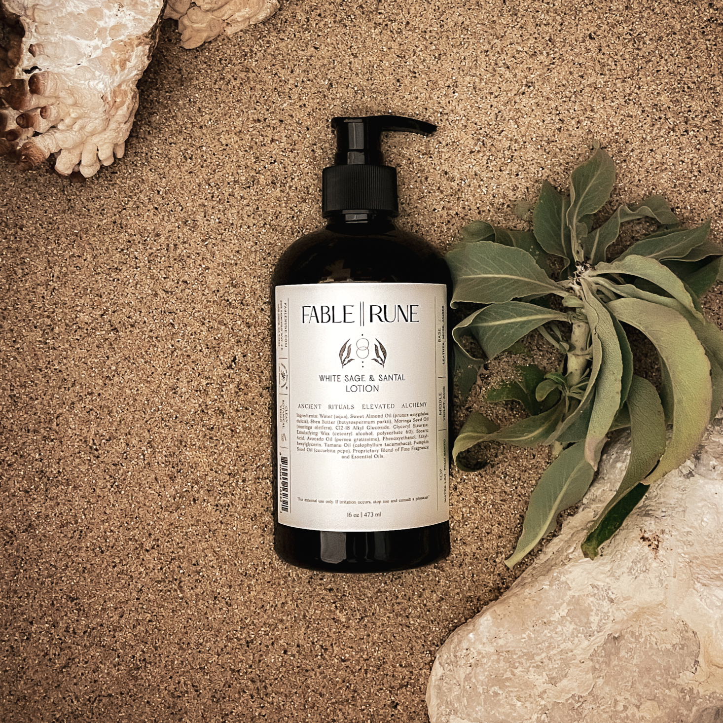 Bottle of Fable & Rune product on sand with a plant and shell