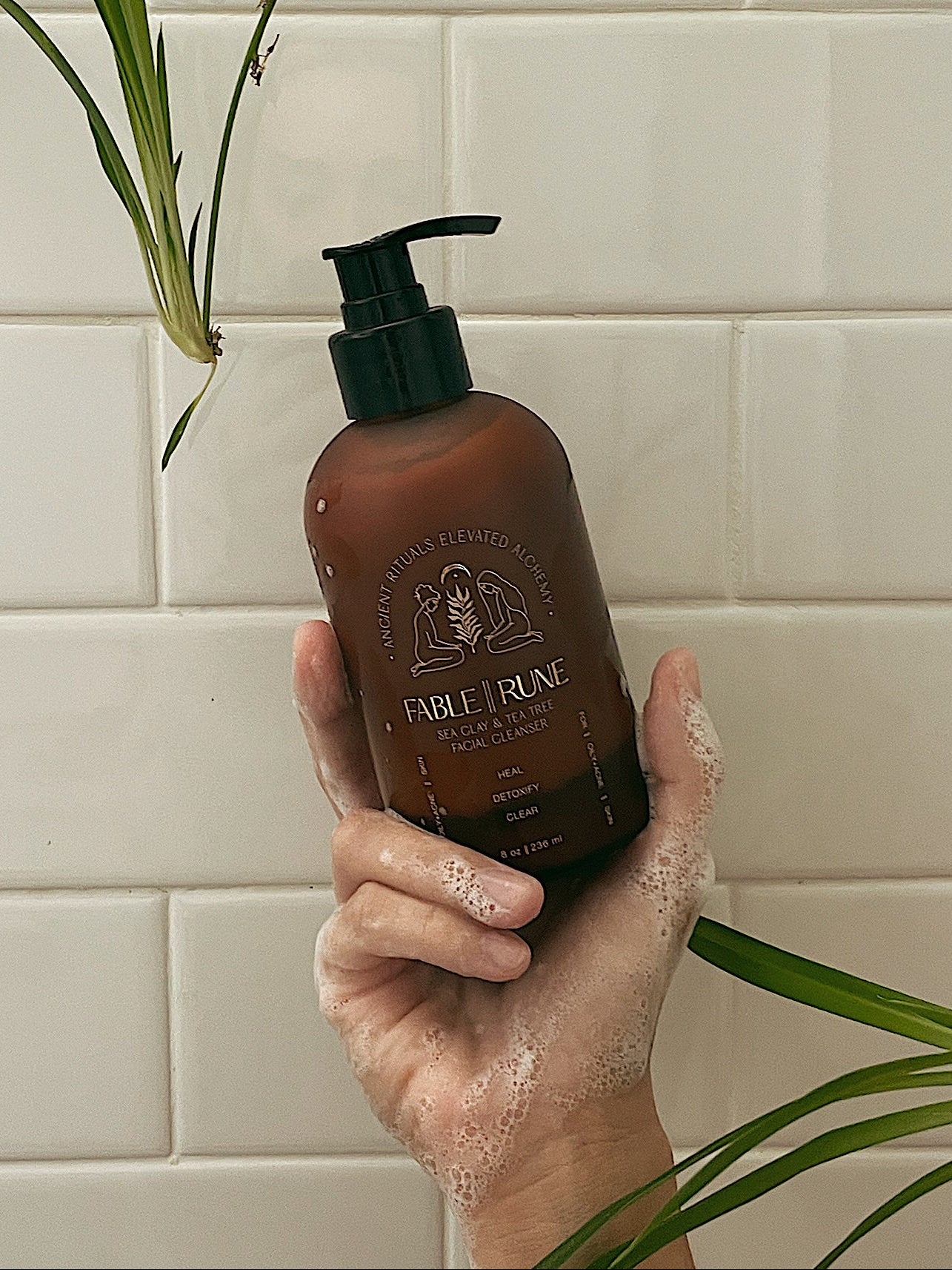 Hand holding a brown bottle labeled 'Fable & Rune' against a tiled bathroom wall.